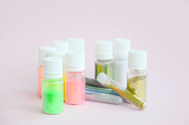 Renkli pırıltılar pastel pembe arka plan üzerinde yatıyor. Oje için çok renkli parlak ışıltılar ile birçok yuvarlak kavanoz. Köpüklü payetler