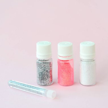 Renkli pırıltılar pastel pembe arka plan üzerinde yatıyor. Oje için çok renkli parlak ışıltılar ile birçok yuvarlak kavanoz. Köpüklü payetler