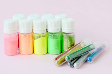 Renkli pırıltılar pastel pembe arka plan üzerinde yatıyor. Oje için çok renkli parlak ışıltılar ile birçok yuvarlak kavanoz. Köpüklü payetler