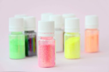 Renkli pırıltılar pastel pembe arka plan üzerinde yatıyor. Oje için çok renkli parlak ışıltılar ile birçok yuvarlak kavanoz. Köpüklü payetler