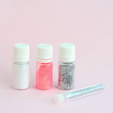 Renkli pırıltılar pastel pembe arka plan üzerinde yatıyor. Oje için çok renkli parlak ışıltılar ile birçok yuvarlak kavanoz. Köpüklü payetler