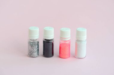 Renkli pırıltılar pastel pembe arka plan üzerinde yatıyor. Oje için çok renkli parlak ışıltılar ile birçok yuvarlak kavanoz. Köpüklü payetler
