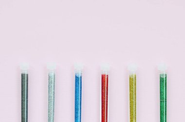 Renkli pırıltılar pastel pembe arka plan üzerinde yatıyor. Oje için çok renkli parlak ışıltılar ile birçok uzun şişe. Köpüklü payetler