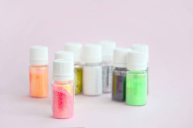 Renkli pırıltılar pastel pembe arka plan üzerinde yatıyor. Oje için çok renkli parlak ışıltılar ile birçok yuvarlak kavanoz. Köpüklü payetler