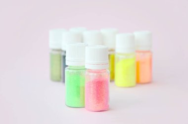 Renkli pırıltılar pastel pembe arka plan üzerinde yatıyor. Oje için çok renkli parlak ışıltılar ile birçok yuvarlak kavanoz. Köpüklü payetler