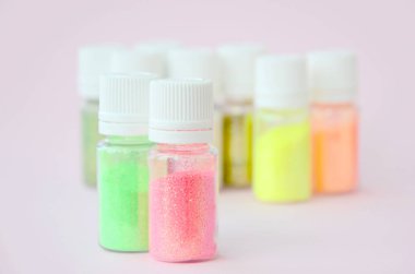 Renkli pırıltılar pastel pembe arka plan üzerinde yatıyor. Oje için çok renkli parlak ışıltılar ile birçok yuvarlak kavanoz. Köpüklü payetler