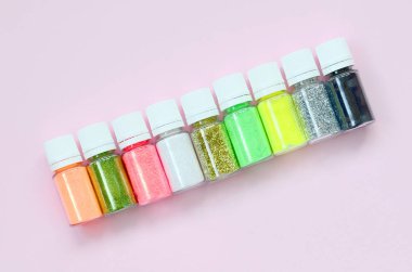 Renkli pırıltılar pastel pembe arka plan üzerinde yatıyor. Oje için çok renkli parlak ışıltılar ile birçok yuvarlak kavanoz. Köpüklü payetler