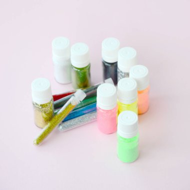 Renkli pırıltılar pastel pembe arka plan üzerinde yatıyor. Oje için çok renkli parlak ışıltılar ile birçok yuvarlak kavanoz. Köpüklü payetler