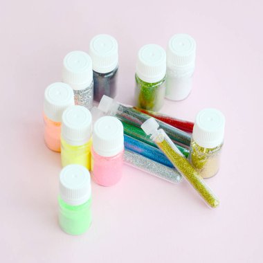 Renkli pırıltılar pastel pembe arka plan üzerinde yatıyor. Oje için çok renkli parlak ışıltılar ile birçok yuvarlak kavanoz. Köpüklü payetler