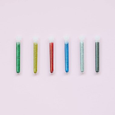 Renkli pırıltılar pastel pembe arka plan üzerinde yatıyor. Oje için çok renkli parlak ışıltılar ile birçok uzun şişe. Köpüklü payetler