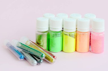 Renkli pırıltılar pastel pembe arka plan üzerinde yatıyor. Oje için çok renkli parlak ışıltılar ile birçok yuvarlak kavanoz. Köpüklü payetler