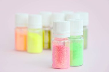 Renkli pırıltılar pastel pembe arka plan üzerinde yatıyor. Oje için çok renkli parlak ışıltılar ile birçok yuvarlak kavanoz. Köpüklü payetler