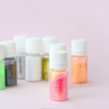 Renkli pırıltılar pastel pembe arka plan üzerinde yatıyor. Oje için çok renkli parlak ışıltılar ile birçok yuvarlak kavanoz. Köpüklü payetler
