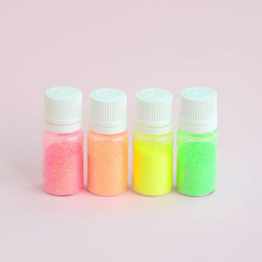 Renkli pırıltılar pastel pembe arka plan üzerinde yatıyor. Oje için çok renkli parlak ışıltılar ile birçok yuvarlak kavanoz. Köpüklü payetler