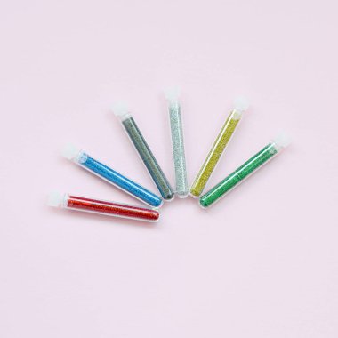 Renkli pırıltılar pastel pembe arka plan üzerinde yatıyor. Oje için çok renkli parlak ışıltılar ile birçok uzun şişe. Köpüklü payetler