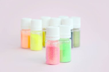 Renkli pırıltılar pastel pembe arka plan üzerinde yatıyor. Oje için çok renkli parlak ışıltılar ile birçok yuvarlak kavanoz. Köpüklü payetler