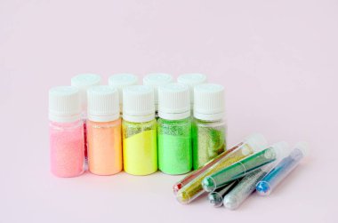 Renkli pırıltılar pastel pembe arka plan üzerinde yatıyor. Oje için çok renkli parlak ışıltılar ile birçok yuvarlak kavanoz. Köpüklü payetler