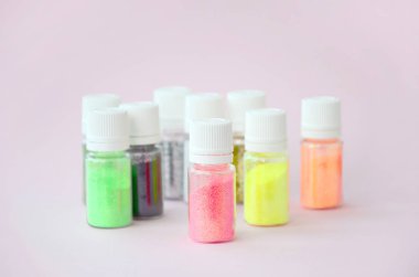 Renkli pırıltılar pastel pembe arka plan üzerinde yatıyor. Oje için çok renkli parlak ışıltılar ile birçok yuvarlak kavanoz. Köpüklü payetler