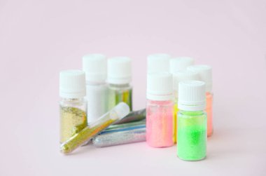 Renkli pırıltılar pastel pembe arka plan üzerinde yatıyor. Oje için çok renkli parlak ışıltılar ile birçok yuvarlak kavanoz. Köpüklü payetler