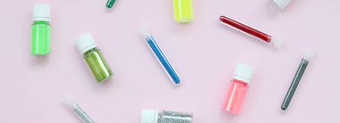 Renkli pırıltılar pastel pembe arka plan üzerinde yatıyor. Oje için çok renkli parlak ışıltılar ile birçok yuvarlak kavanoz. Köpüklü payetler