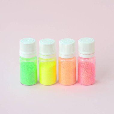 Renkli pırıltılar pastel pembe arka plan üzerinde yatıyor. Oje için çok renkli parlak ışıltılar ile birçok yuvarlak kavanoz. Köpüklü payetler