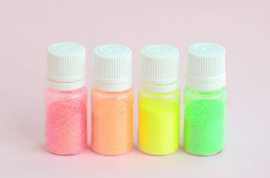 Renkli pırıltılar pastel pembe arka plan üzerinde yatıyor. Oje için çok renkli parlak ışıltılar ile birçok yuvarlak kavanoz. Köpüklü payetler