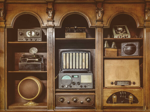 Sepia toned image of old radio 's in a wooden cabinet
