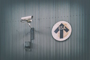 Surveillance camera with vintage USA direction sign on a steel wall clipart