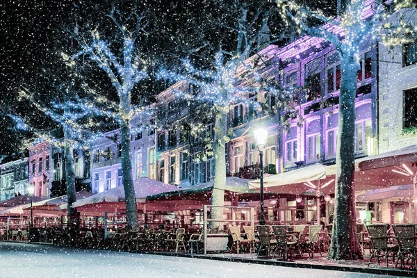Bars and restaurants with christmas lights on the famous Vrijthof square in Maastricht during snowfall, The Netherlands