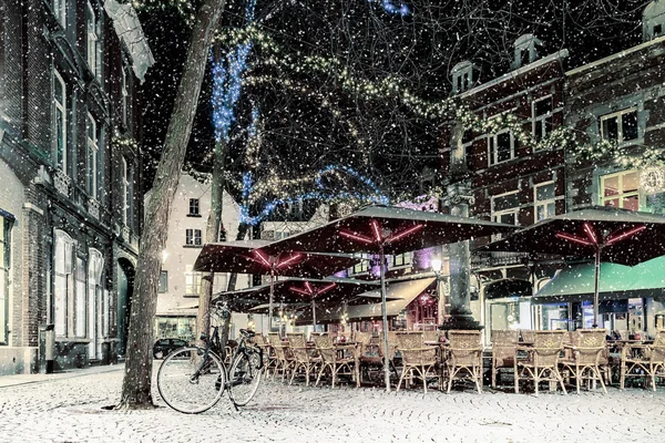 Bars and restaurants with christmas lights on the Sint Amorsplein square in Maastricht during snowfall, The Netherlands