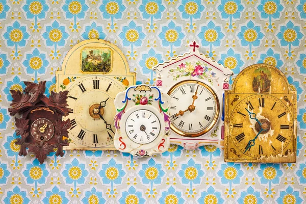 Collection of colorful hanging clocks in front of retro wallpape