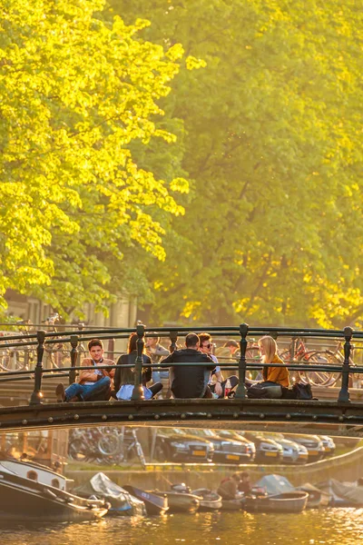 Jugendliche entspannen sich bei Sonnenuntergang auf einer Amsterdam-Kanalbrücke — Stockfoto