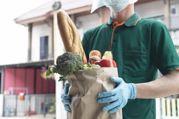 Yeşil gömlekli servis elemanı, kapıdaki müşteriye taze yiyecek çantası taşıyor.