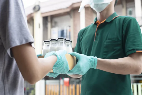 Yeşil üniformalı adam yemek kutusuna süt şişesi koyuyor. 