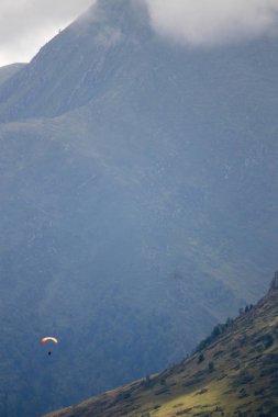 Paraşütçü adam dağların arasında uçuyor.