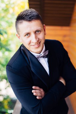 Siyah smokin bir papyon ile yakışıklı damat portresi, o Balkonda duran, kameraya bakıyor ve gülümsüyor.