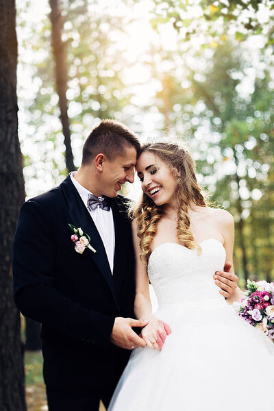 Great portrait of a wedding couple, which is walking in the park. They are holding their hands, standing face to face and smiling.