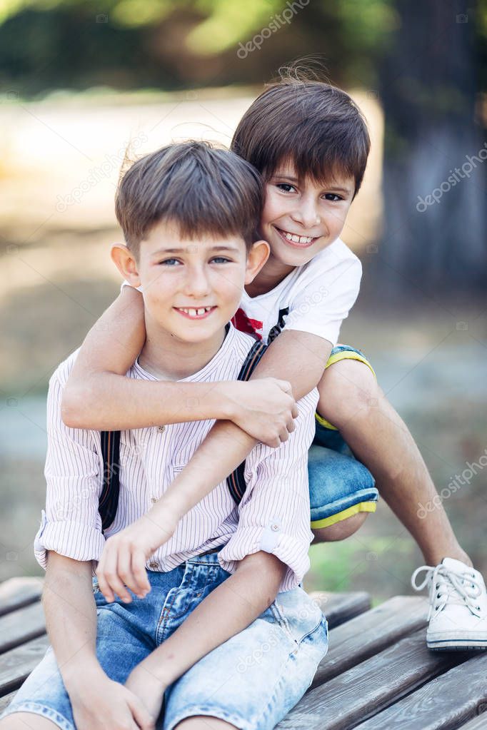 Portrait of a two little brothers. They are sitting in the park, embracing and smiling.