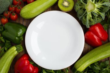 Boş beyaz tabak, sebze ve meyve kahverengi zemin üzerinde. Sağlıklı gıda maddeleri. Üstten görünüm. Kopya alanı.