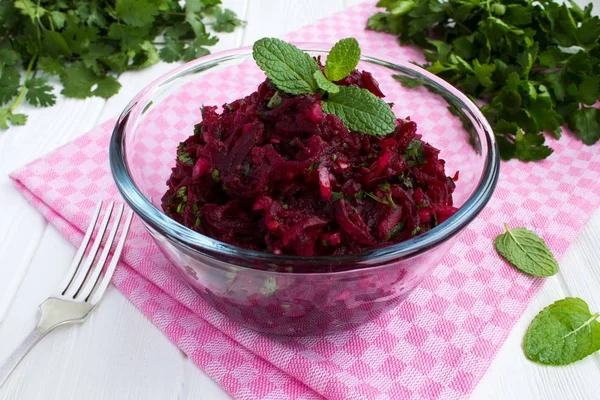 Salad with grated beets and herbs in the glass bowl on the white wooden  background