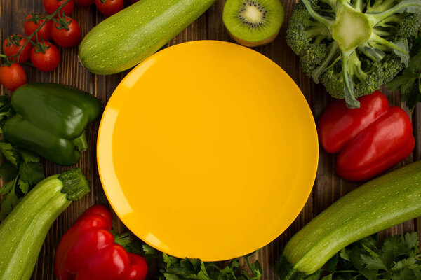 Empty yellow plate, vegetables and fruit on the brown background.Healthy food ingredients.Top view.Copy space.