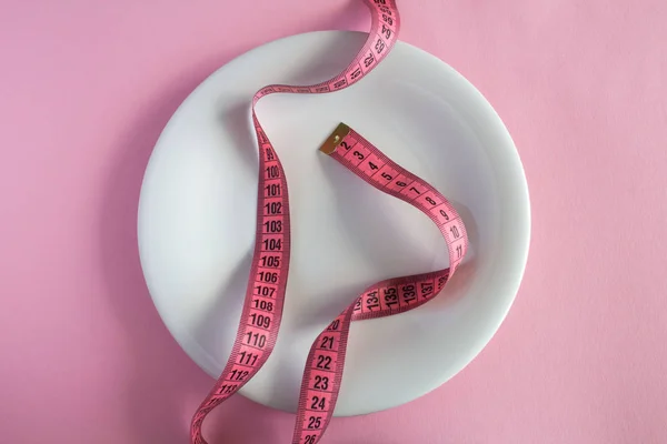 White plate and centimeter  on the pink  background.Top view.Diet minimal concept.