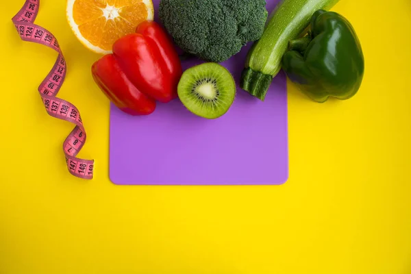 Vegetables,fruits and pink centimeter on the violet  cutting board  on the yellow background.Top view.Copy space.