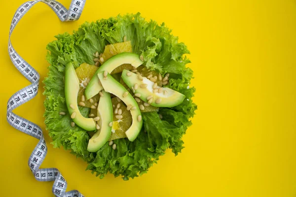 Vegetarian salad with avocado, lettuce leaves, orange and pine nuts  on the yellow background.Top view.Copy space.