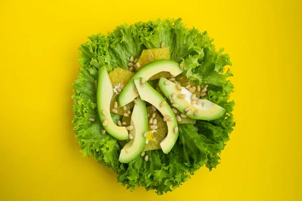 Vegetarian salad with avocado, lettuce leaves, orange and pine nuts  on the yellow background.Top view.