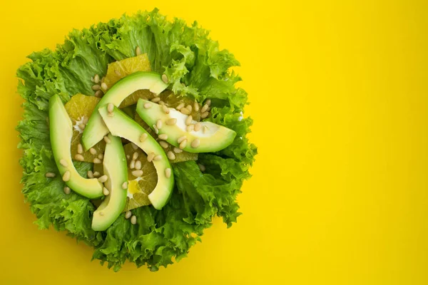 Vegetarian salad with avocado, lettuce leaves, orange and pine nuts  on the yellow background.Top view.Copy space.