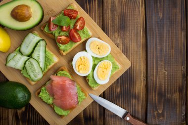 Sandviç kahverengi ahşap zemin üzerinde avokado ve farklı malzemelerle. Üstten görünüm. Kopya alanı.