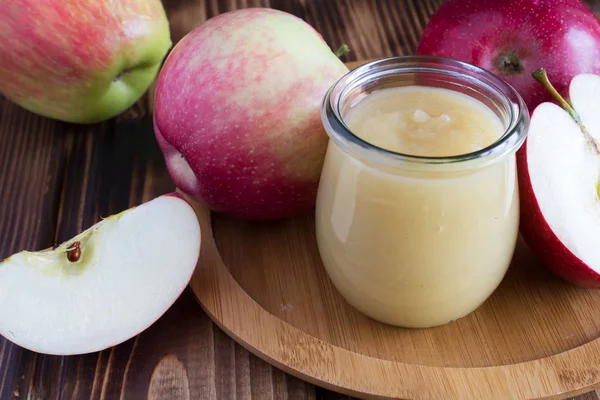 Apples puree in the jar and red apples on the wooden cutting board