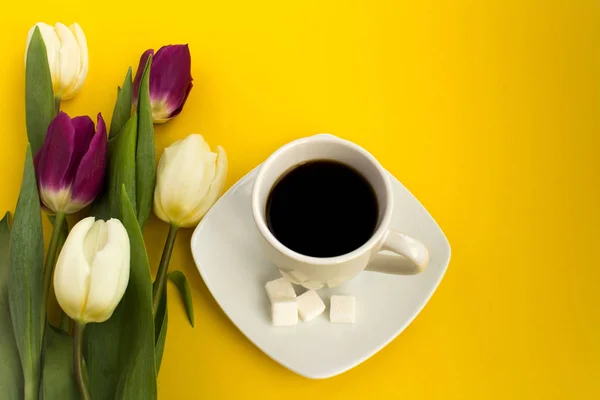 Cup of coffee and tulips on the yellow background. Top view.