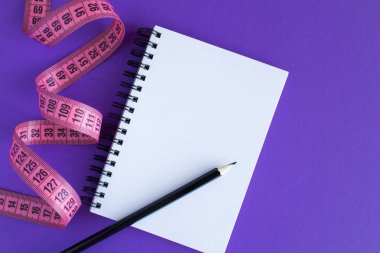 Pink santimetre ve mor zemin üzerine açık not etmek. Üstten görünüm. Diyet en az kavramı. Kopya alanı.